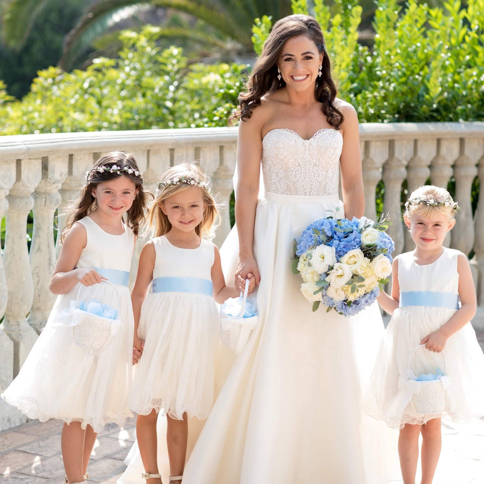 Bride and three cute flower girls in light ivory wedding dresses with blue belts